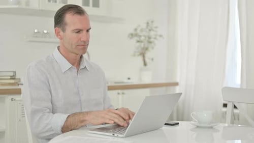 Serious Middle Aged Man Using Laptop at Home