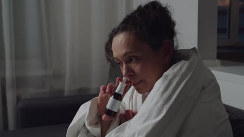 Portrait d'une femme malade dans une couverture enveloppée utilisant un spray nasal à l'intérieur