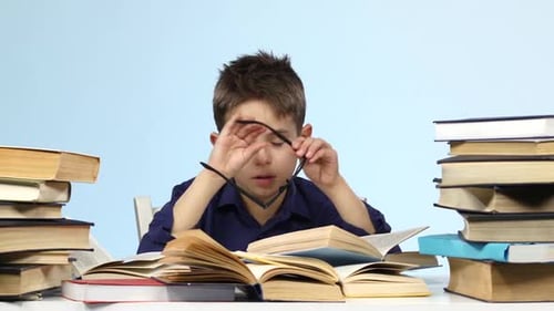 Leepy Little Boy sitzt an einem Tisch und blättert müde durch ein Buch. Blauer Hintergrund.