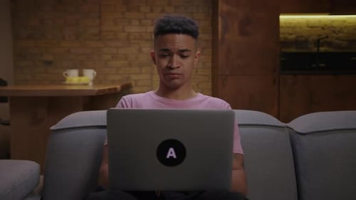 Young Adult African American Man Working Typing on Laptop Sitting on Couch at Home Remote Office