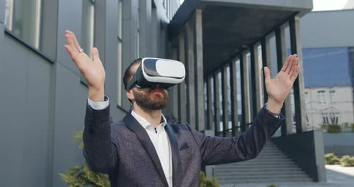 Man in Virtual Reality Headset Working on Imaginary Screen Near Modern Urban building