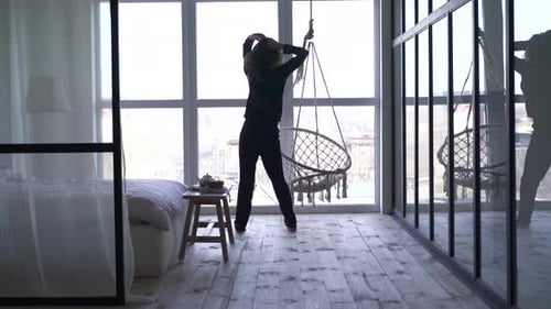 Cheerful Caucasian Woman Dancing and Spinning in Front of Big Window in Bedroom. Back View of