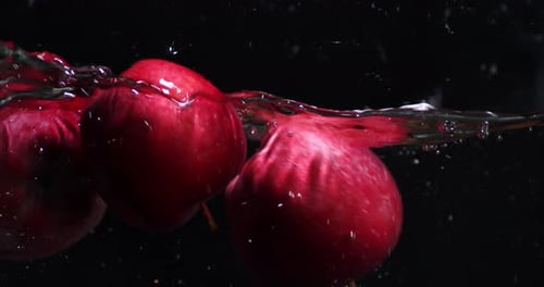 Des pommes rouges fraîches tombent dans l'eau.