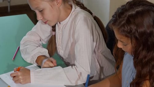 Young Girls Drawing Together Indoors with Colored Pencils