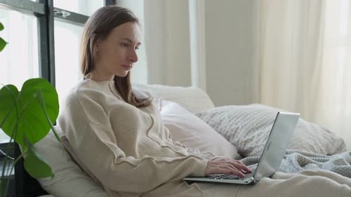 Woman Working on Laptop While Relaxing on Bed