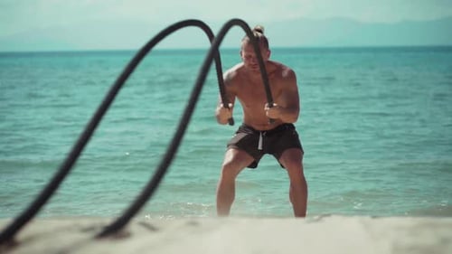 Mann trainiert mit Battle Rope am Strand