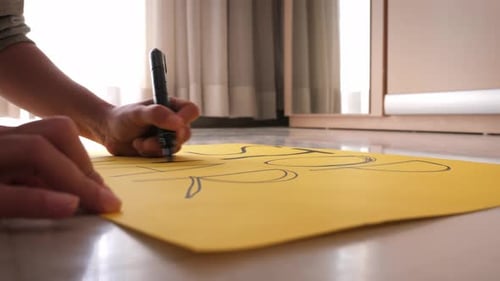 Person Drawing on Yellow Paper with Marker
