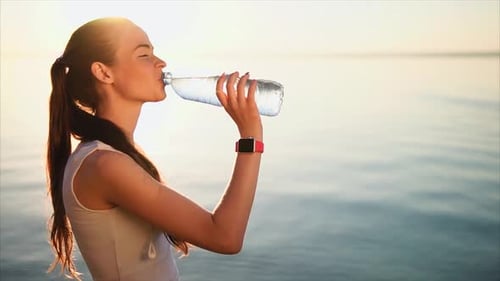Young Brunette Woman Drinking a Water From the Plastic Bottle Near the Sea