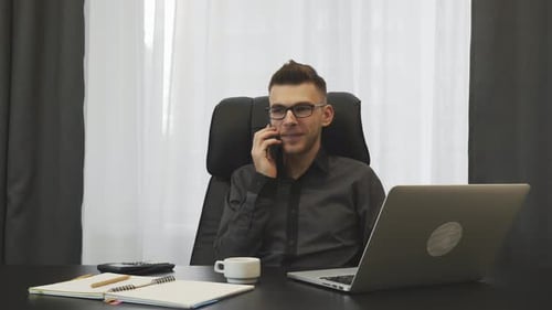 Successful young businessman talking on phone in his modern office