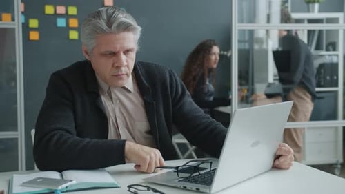 Slow Motion of Sleepy Guy Napping on Desktop Then Waking Up and Working with Laptop in Office