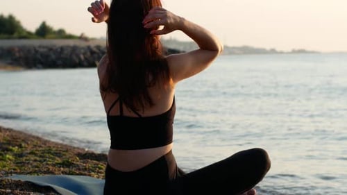 Une femme yogi est assise en position de lotus au bord de la mer et regarde l'aube du soleil.