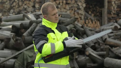 Lumberjack in Reflective Jacket. Man Woodcutter with Electric Chainsaw. Sawn Logs, Firewood, Sawmill