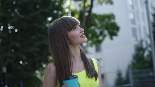 Pretty Girl with Glass of Beverage Admiring the Environment During a Walk
