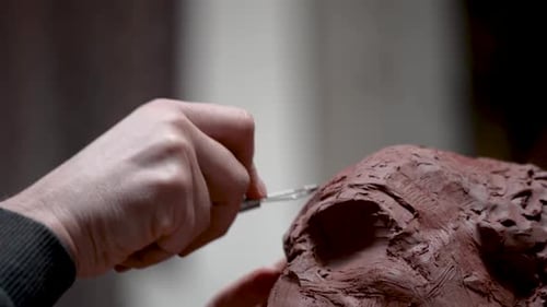 Hands Sculpting Clay with Tool in Dimly Lit Studio