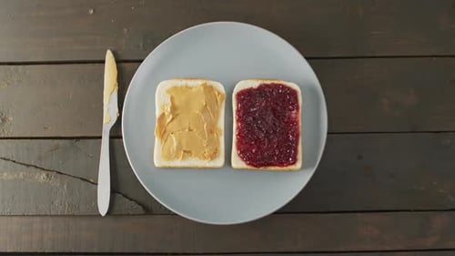 Close up view of peanut butter and jelly sandwich in a plate with butter knife on wooden surface