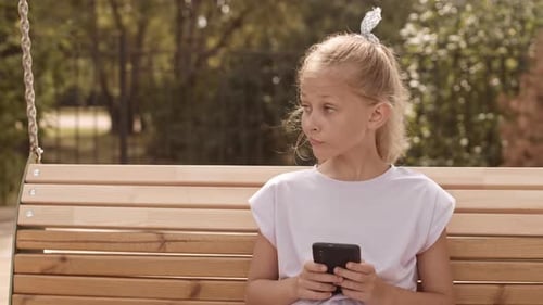 Girl Using Smartphone on Swing in Park