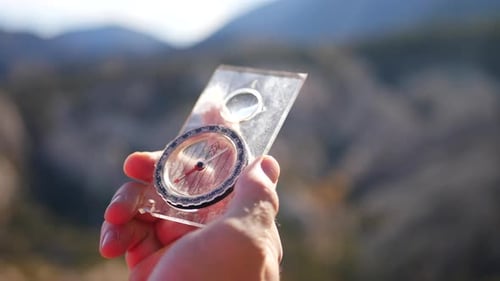 Close up on a hand holding a scratched magnetic compass with the epic forest and mountains of califo