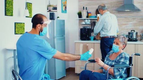 Caregiver Giving Pills to Senior Woman in Wheelchair