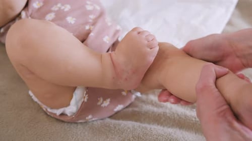 Adult Massaging Legs of Baby on Blanket