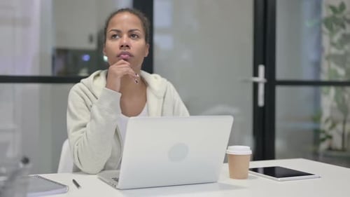 African Woman Thinking While Working on Laptop in Office