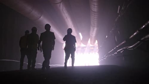 silhouette of many construction workers walking out from a large tunnel