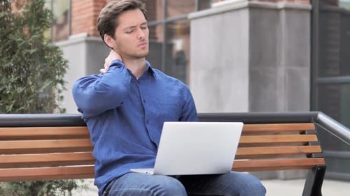 Sitting Outdoor Young Man with Neck Pain Working on Laptop