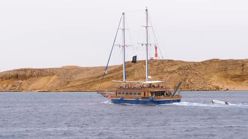 Beautiful Tourist Yacht Sails in the Stormy Sea on the Background of Rocks. Egypt