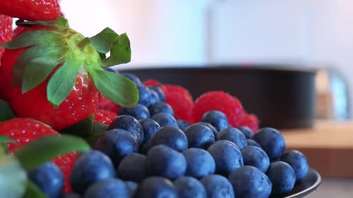 Eine Frau legt Blaubeeren auf einen Erdbeerhaufen in einer Schüssel auf einer Küchentheke