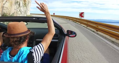 Hipster-Mann mit Hut winkenden Armen fährt im Cabrio auf kurvenreicher Küstenstraße