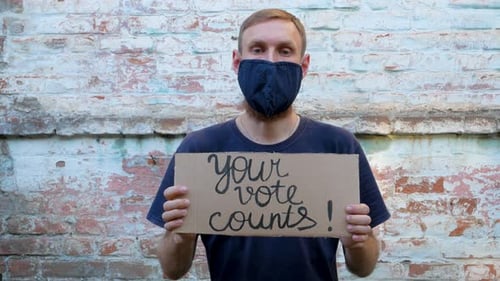 Man Holds Vote Sign and Points to Camera