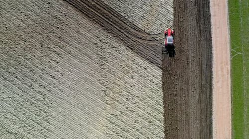Red tractor plowing field on spring, view from drone