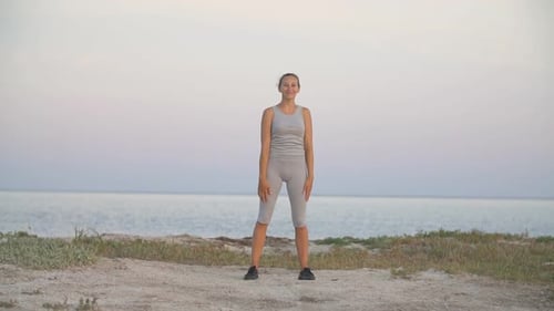 Woman Doing Stretching Exercises by the Ocean at Sunrise