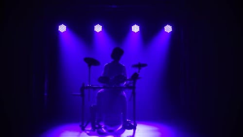 Ein Musiker-Schlagzeuger, der in einem dunklen Studio ein Musikinstrument spielt, vor einem Hintergrund silhouettiert