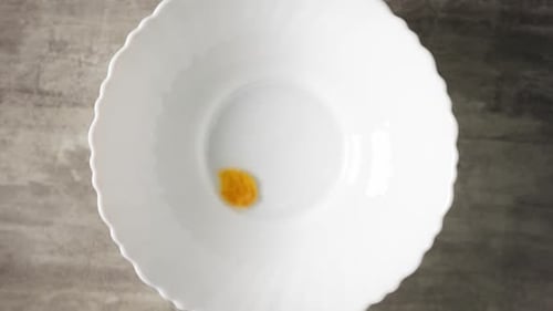 Yellow Cornflakes are Falling From Above Into a White Plate Standing on Wooden Surface in Slowmo