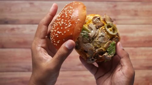 Hand Holding Beef Burger on Table Close Up