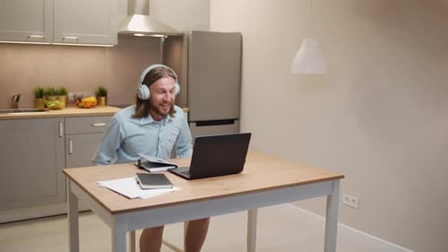 Man with Headphones Video Calling on Laptop in Kitchen