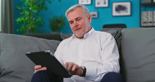 Mature Man Using Tablet Device on Sofa