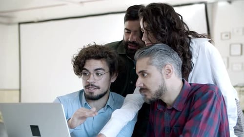 Smiling Coworkers Talking, Gesturing and Looking at Laptop in Office