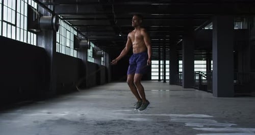 Shirtless african american man skipping the rope in an empty urban building