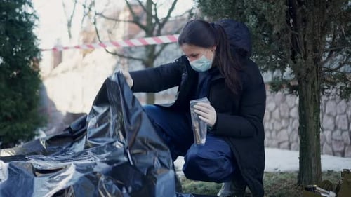 Side View Young Caucasian Female Criminologist Sitting on Hunkers at Crime Scene with Evidence