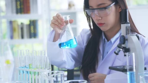 Asian Medical Researcher Working in Pharmacy Laboratory While Mixing Chemical in Flask with Tube