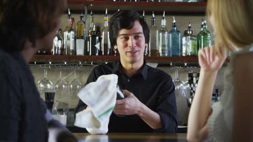 Friendly Bartender Drying Glass and Conversing with Customers