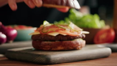 Hands Add the Top Bun to a Cheeseburger