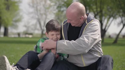 Senior Man Sitting with His Grandson on the Blanket in the Park
