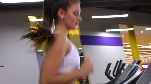 A Young Beautiful Woman Runs on a Treadmill in a Gym