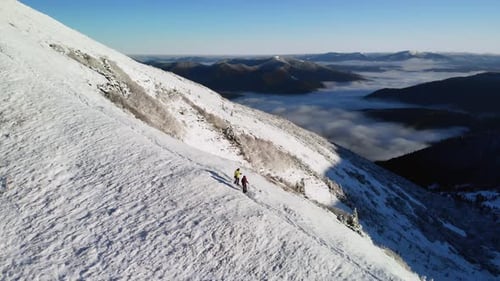 Drone Flying Over Young Couple of Hikers Descending a Mountain Ridge in Winter