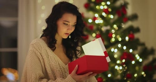 Woman Opens Christmas Present in Front of Tree