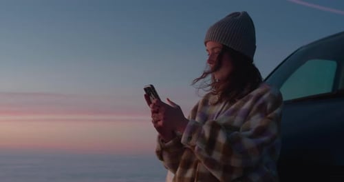 Young Woman Using Phone By Car at Sunset