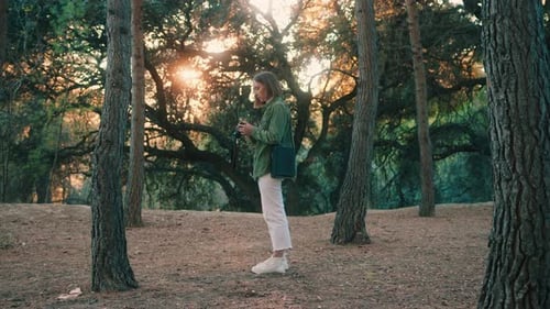 Woman Using Camera in Forest During Sunset