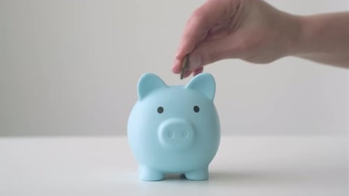Hand Putting Coins Into Piggy Bank
